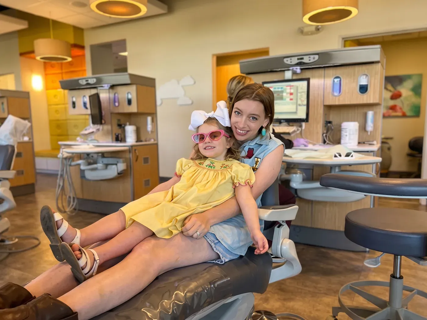 A mother and her daughter in pink sunglasses relaxing together in a dental chair