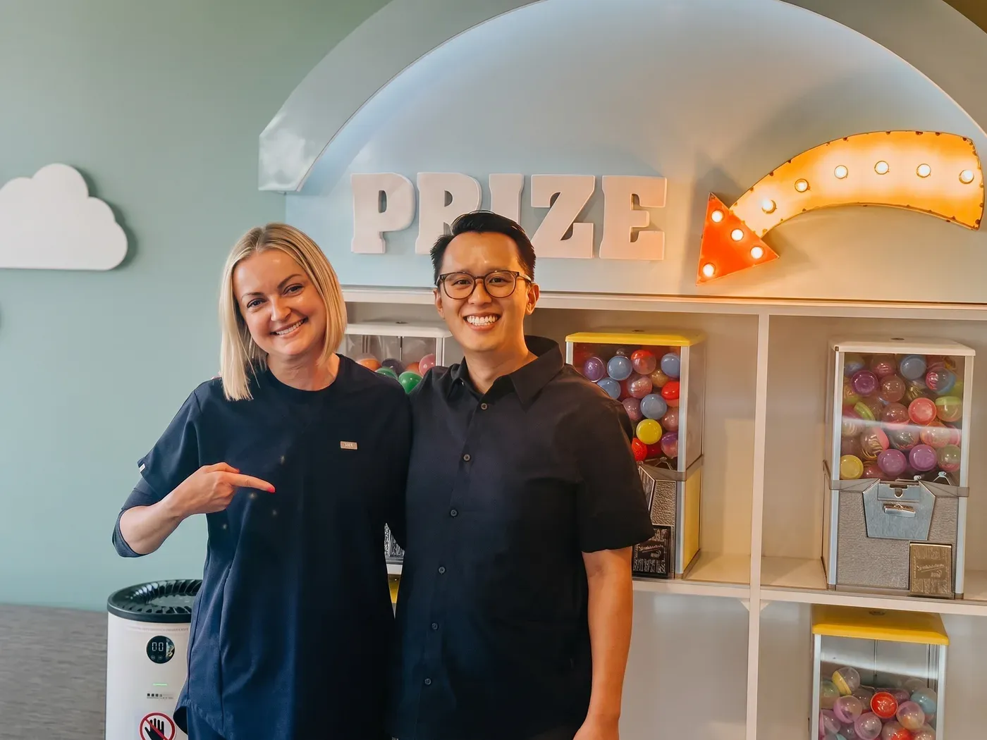 Two Smile Gallery team members smiling in front of the prize wall