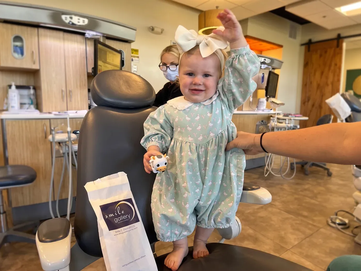 A toddler standing on the dental chair beside her Smile Gallery gift bag