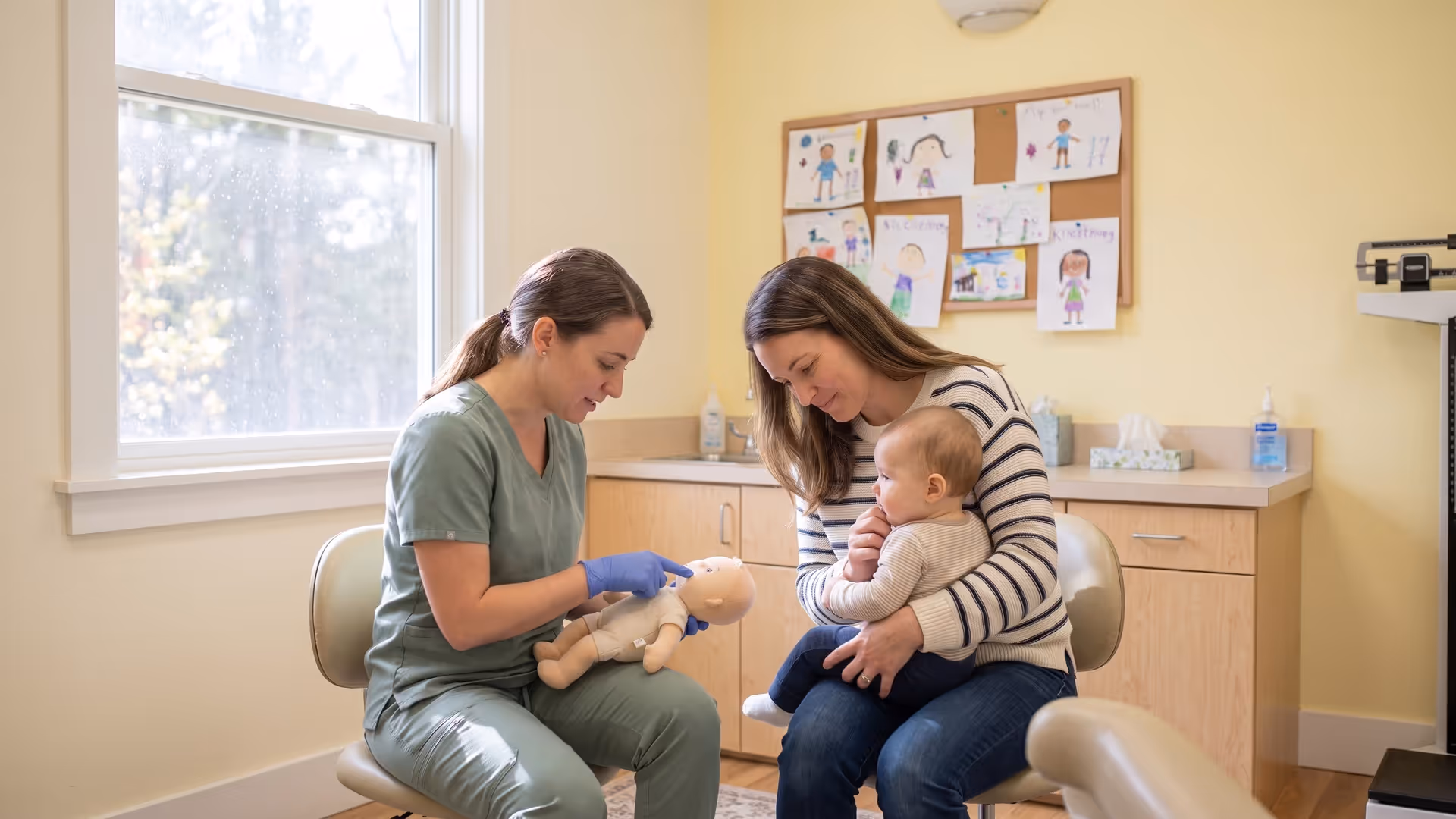 A dental team member showing a mother tongue-tie aftercare stretches on a baby doll while she holds her infant