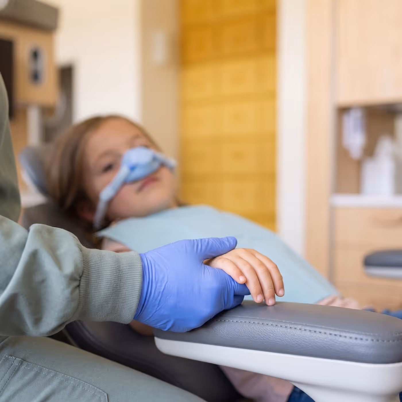 A child's hand held by an assistant during treatment under nitrous