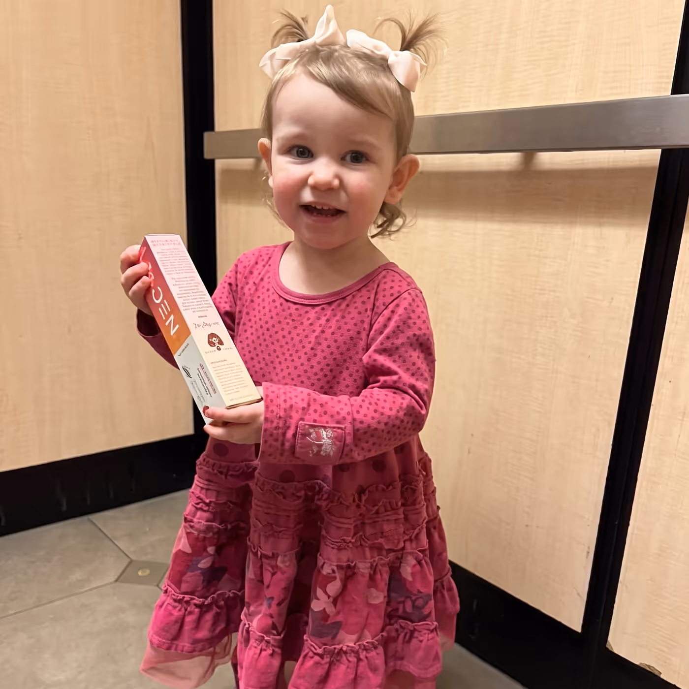 A smiling toddler holding a box of fluoride-free nano-hydroxyapatite kids toothpaste
