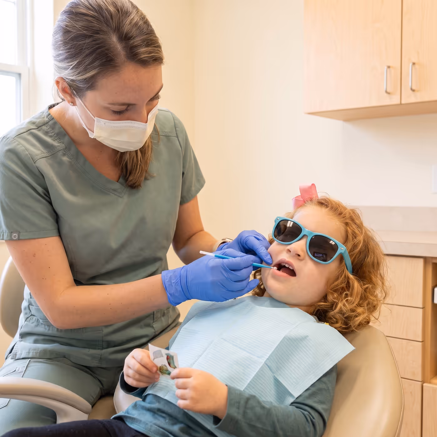 A dental team member painting silver diamine fluoride onto a child's back tooth with a tiny brush, no drilling needed